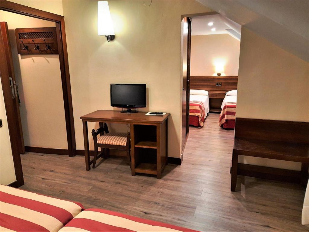 a hotel room with a desk with a television and two beds at Hotel Urogallo in Vielha