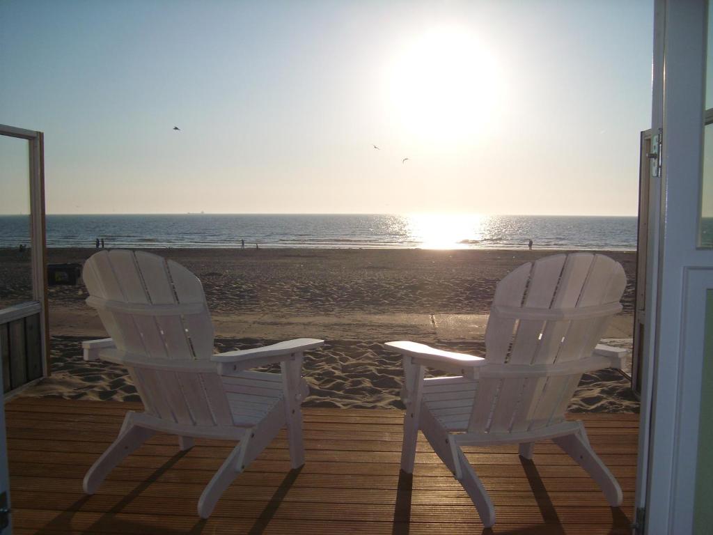 Dos sillas blancas sentadas en un porche con vistas a la playa en Luxe Strandhuisje op het strand van Wijk aan Zee met wifi, en Wijk aan Zee