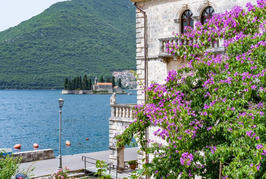 a building with purple flowers next to a body of water at Villa Burovic Historic Beachfront Stone House Perast in Perast