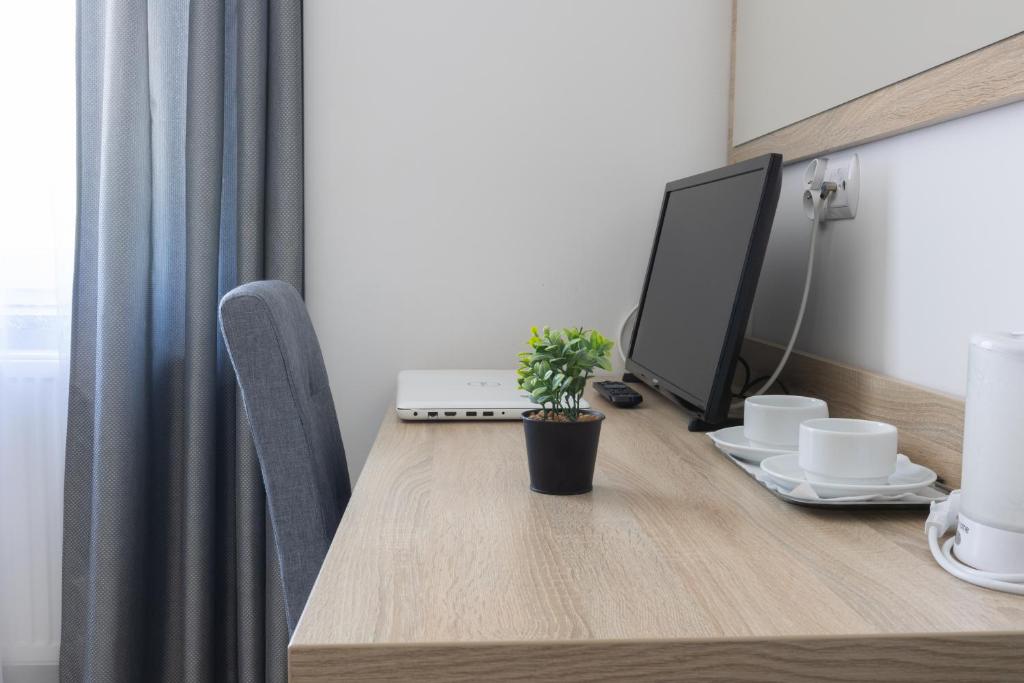 Wooden desk with laptop, small plant, and cups in a minimalist setting.