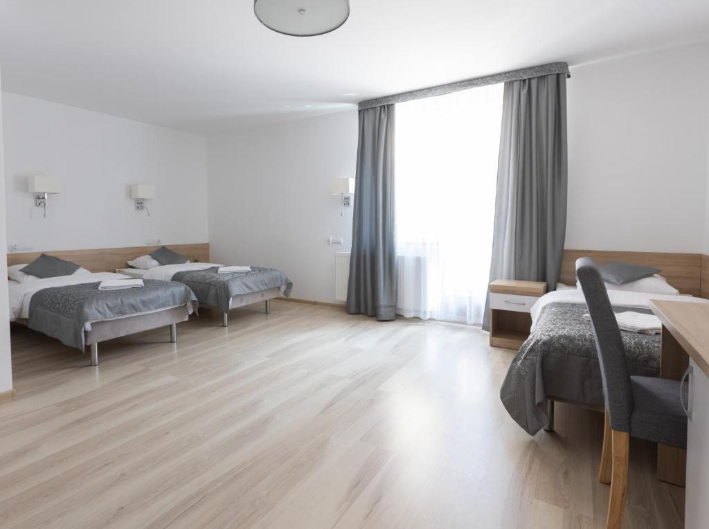 Room with three beds, desk, chair, and large window with curtains.