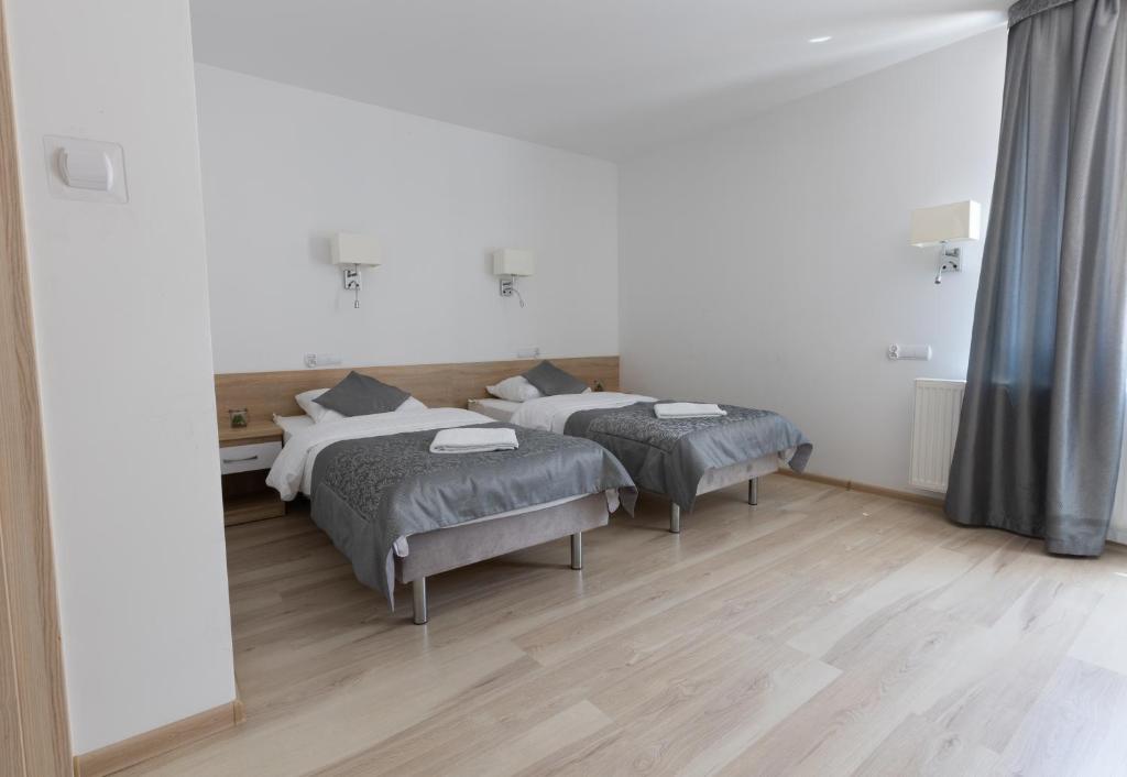 Room with two beds, wooden floor, and large window with curtains.