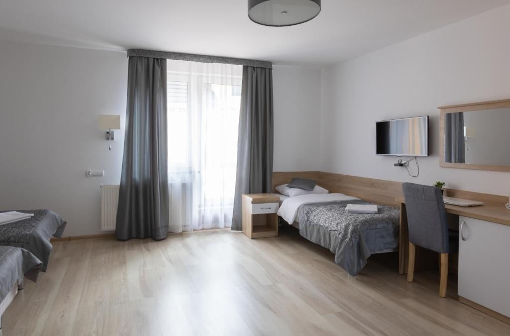 Room with single bed, desk, chair, TV, and large window with curtains.