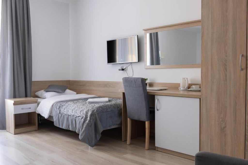 Single bed room with desk, chair, TV, and wooden accents.