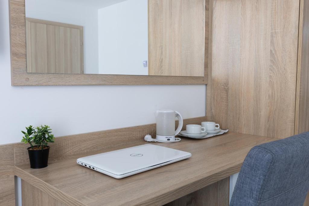 Desk with laptop, kettle, cups, and small plant under a mirror.