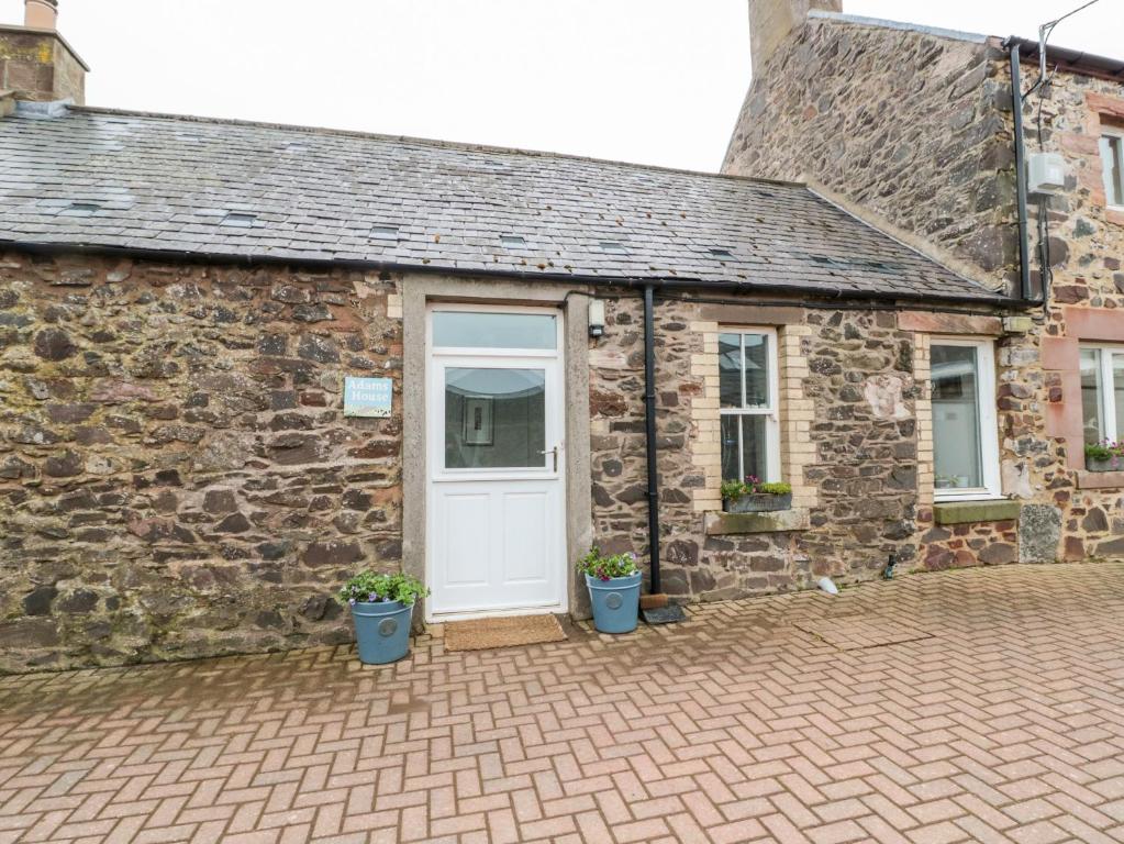 a stone cottage with a white door and two potted plants at Adams House in Eyemouth