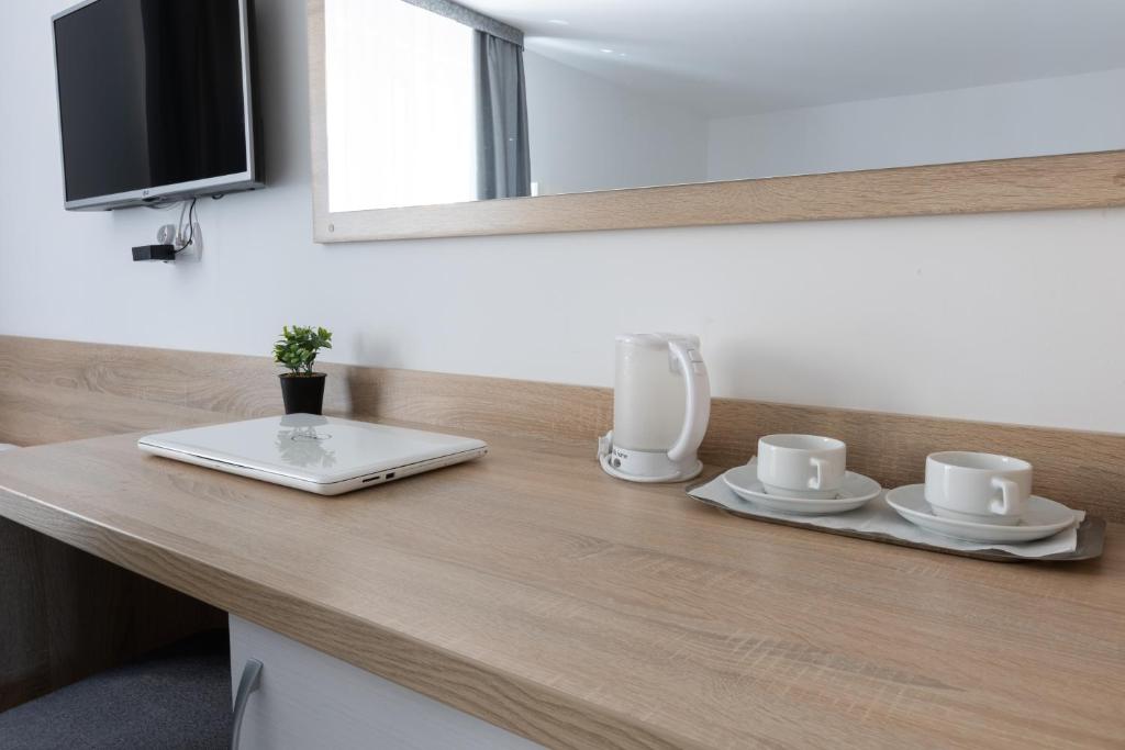 Desk with laptop, cups, kettle, and wall-mounted TV.