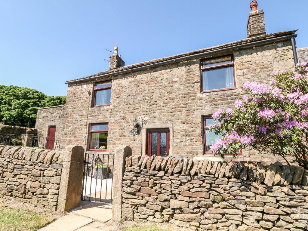 an old stone house with a stone wall at Keepers Cottage in Chapel en le Frith