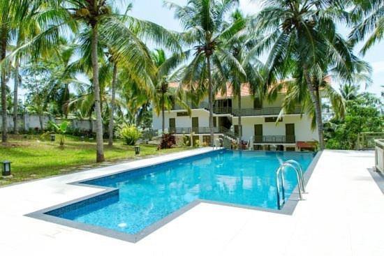 a swimming pool in front of a house with palm trees at Aanandakosha Ayurveda Retreat in Trivandrum