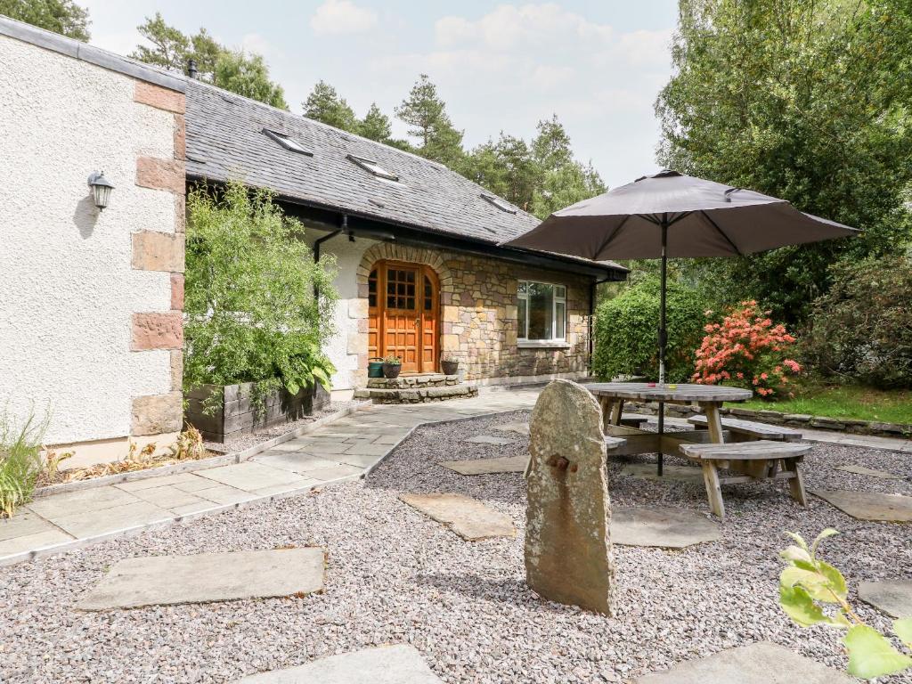 a stone bench and an umbrella in front of a house at Tigh Na Drochit in Garve