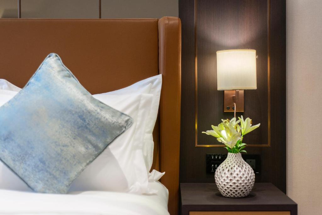 a bed with a pillow and a vase of flowers on a table at Gardino Hotel & Residence in Riyadh