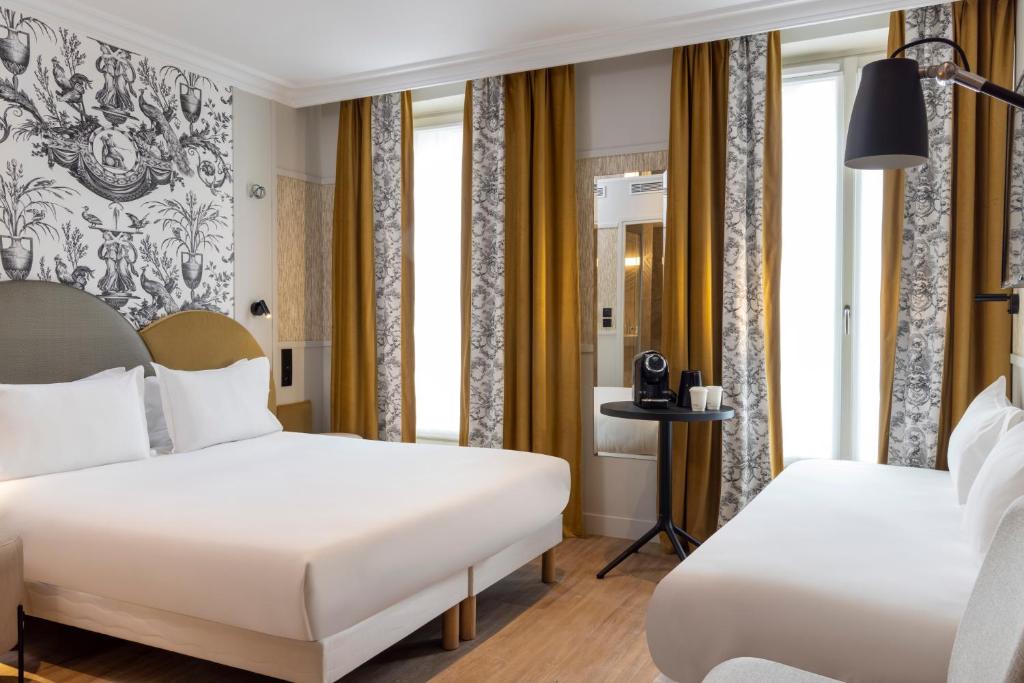 two beds in a hotel room with windows at Grand Hôtel Lévêque in Paris