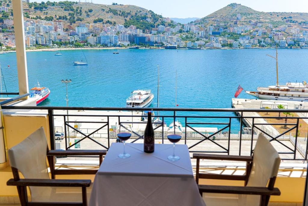 a table with wine glasses on a balcony with a view of the water at Hotel Mano in Sarandë