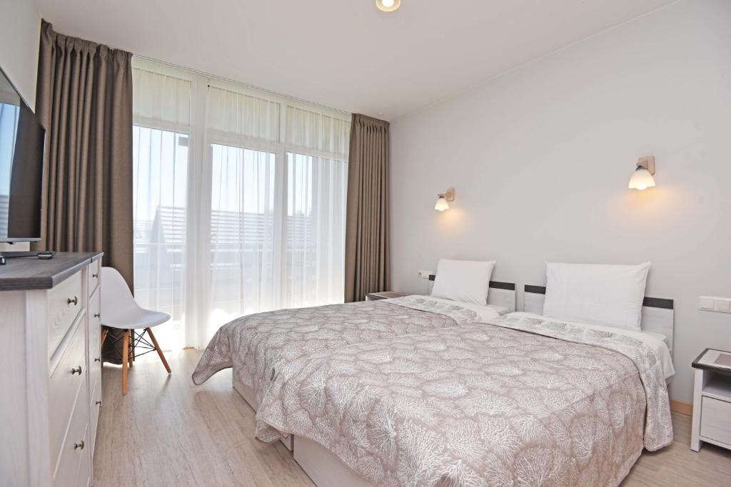 a white bedroom with a bed and a television at Ritos Apartamentai Palangoje in Palanga