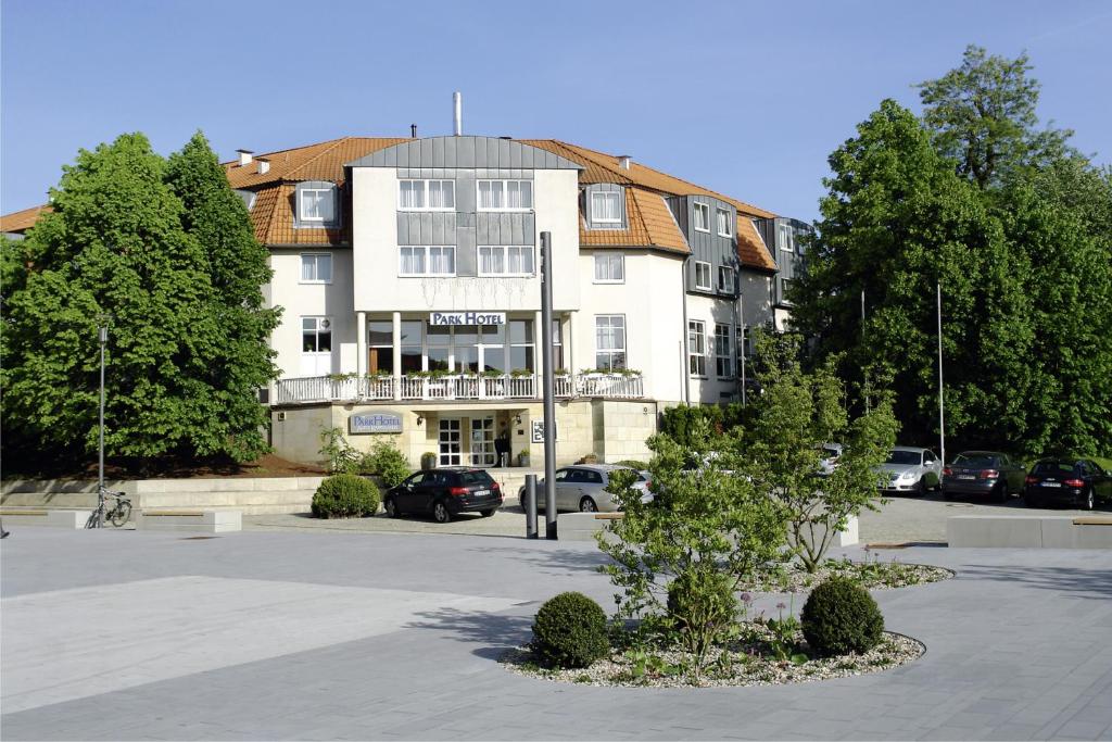 ein großes weißes Gebäude mit Autos auf einem Parkplatz in der Unterkunft Parkhotel Altes Kaffeehaus in Wolfenbüttel