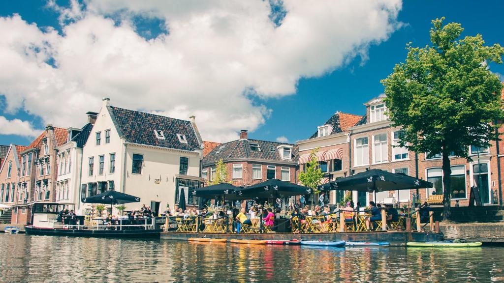 un grupo de personas sentadas en mesas junto a un río en Hotel Café Restaurant 't Raedhûs, en Dokkum