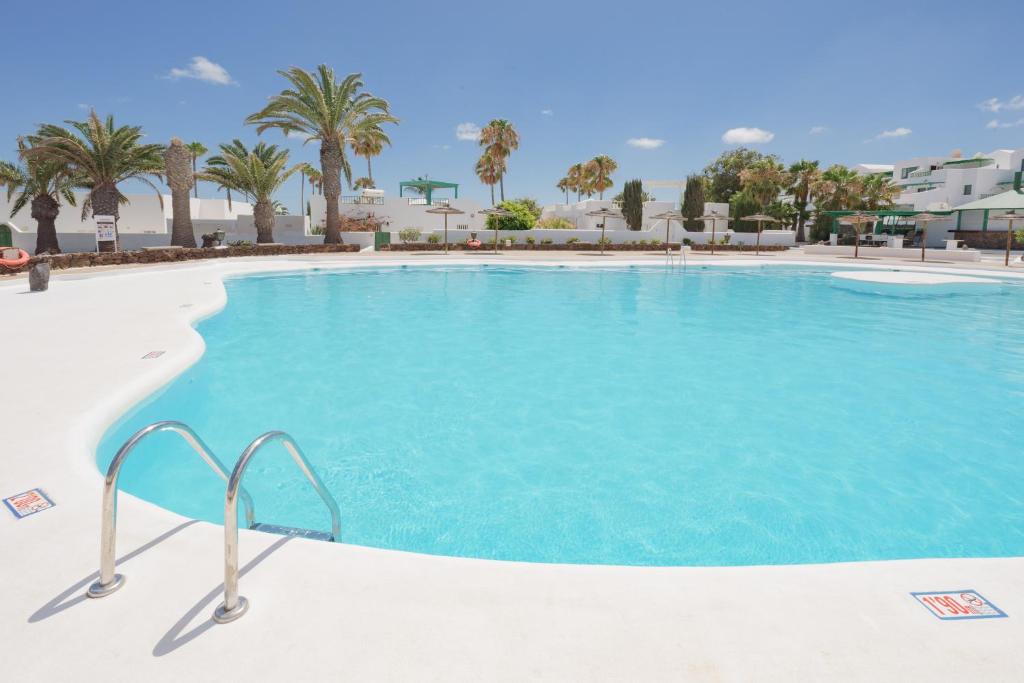 een groot zwembad met blauw water en palmbomen bij Lanzahost Apartamento LARIMAR in Costa Teguise
