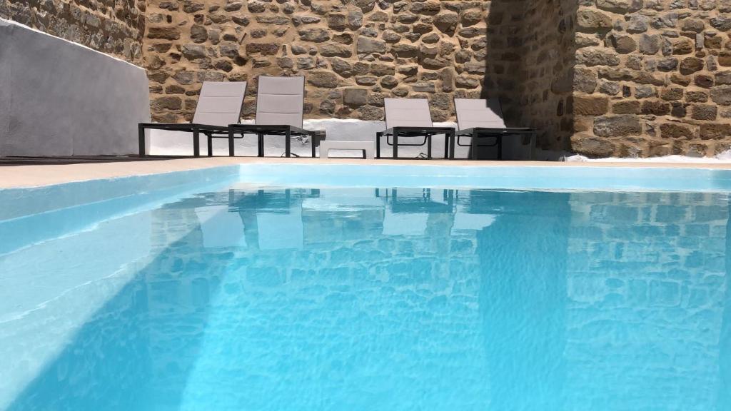 a swimming pool with three chairs next to a stone wall at YIT El Postigo in Úbeda