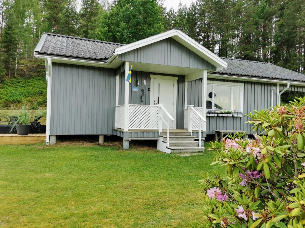 a small grey house with a porch and a yard at Stuga Solbacken nära Rådasjön in Råda