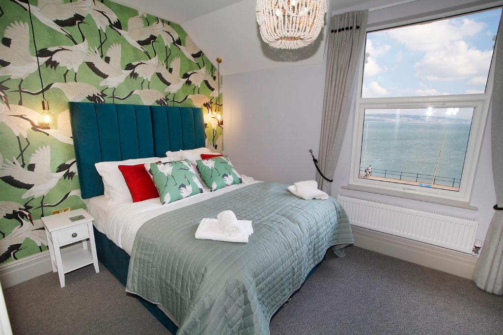 sypialnia z łóżkiem z niebieskim zagłówkiem i oknem w obiekcie Sea Watch Seafront Holiday House w mieście The Mumbles