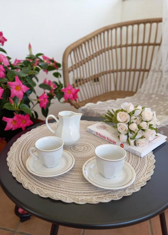 a table with two tea cups and a book and flowers at B&B Drusilla in Fondi
