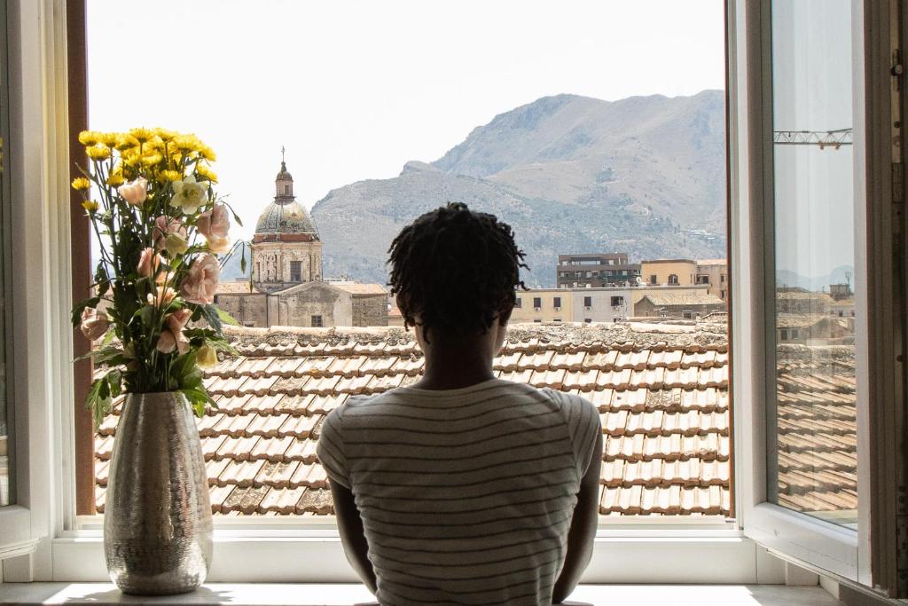 una persona seduta davanti a una finestra con un vaso di fiori di Sopramoltivolti a Palermo