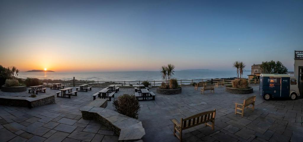 a patio with benches and tables and the ocean at sunset at Shoreline Hotel in Donabate