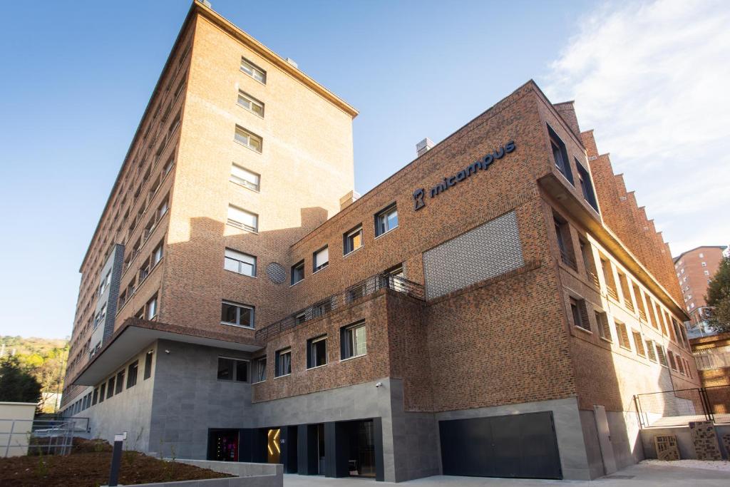 un edificio de ladrillo marrón con un cartel azul en micampus Bilbao Student Residence, en Bilbao