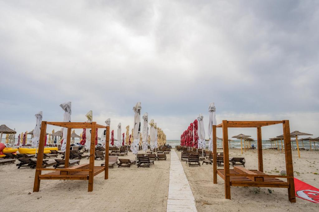 une plage de sable avec des chaises, des parasols et des tables dans l'établissement Home Space One, à Mamaia Nord – Năvodari