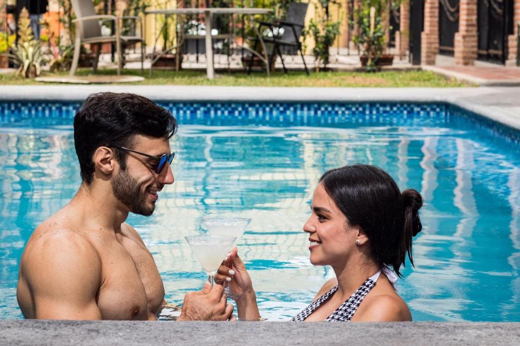 un homme et une femme assis dans une piscine avec un verre dans l'établissement Hotel Boutique Sol y Luna SPA, à Ajijic