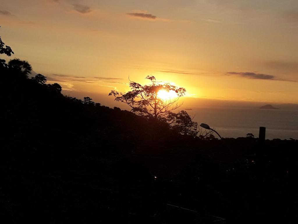 una puesta de sol en una colina con un árbol en Chale Por do Sol, en Ilhabela