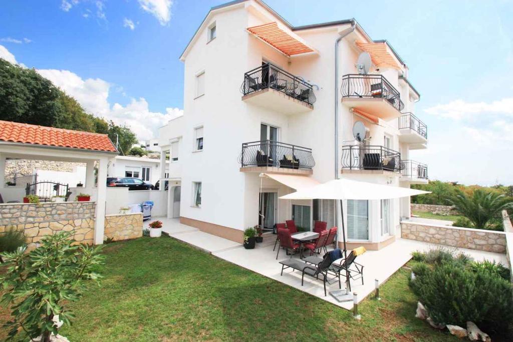 a white house with a patio with chairs and an umbrella at Apartments in Crikvenica 39076 in Sopaljska