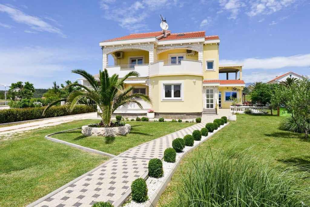 een groot geel huis met een palmboom in de tuin bij Apartment in Ljubac/Zadar Riviera 31380 in Ljubač