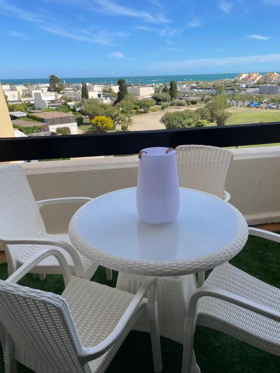 une table et des chaises blanches sur un balcon avec une tasse dans l'établissement SHOWTIME NATURISTE PORT NATURE 6 parking privé clim ascenseur vue mer, au Cap d'Agde