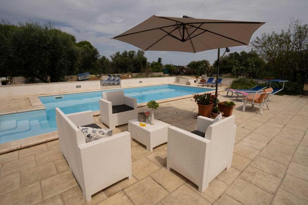 een patio met een parasol en stoelen en een zwembad bij VILLA TIMEA in Castrignano del Capo
