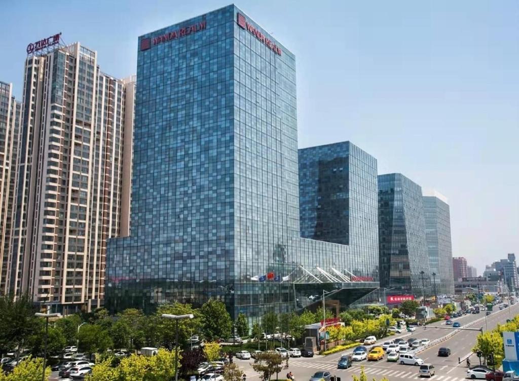 a tall glass building with cars in a city at Wanda Realm Langfang in Langfang