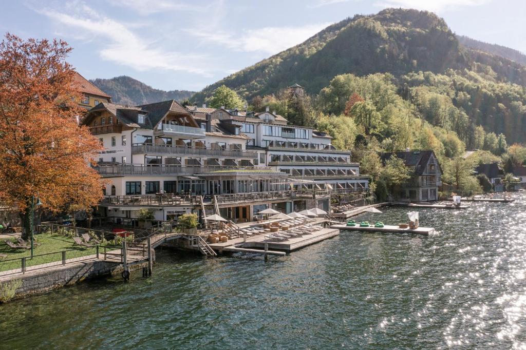 a hotel on a river with mountains in the background at Das Traunsee - Das Hotel zum See in Traunkirchen