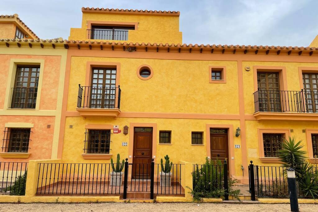 una casa amarilla con una valla delante de ella en ELEGANTE DÚPLEX EN DESERT SPRINGS GOLF RESORT, en Cuevas del Almanzora