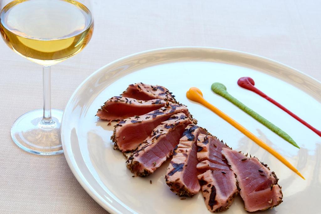 a plate with a piece of meat and a glass of wine at Hotel Baia Imperiale in Campo nell'Elba