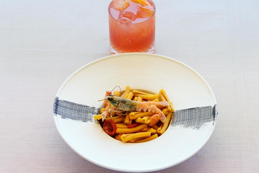 a plate of pasta with shrimp and vegetables and a drink at Hotel Baia Imperiale in Campo nell'Elba