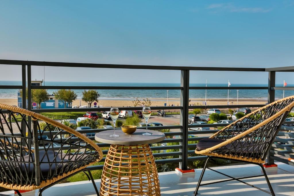 een balkon met een tafel en stoelen en het strand bij Hôtel & Spa FACE À LA MER in Merville-Franceville-Plage