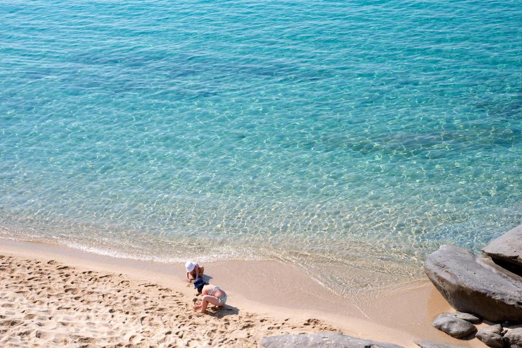 two people standing on a beach near the water at Hotel Baia Imperiale in Campo nell'Elba