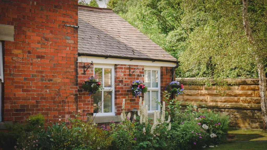 a small red brick house with flowers on the window at River Cottage at Old Post Office in Bardon Mill