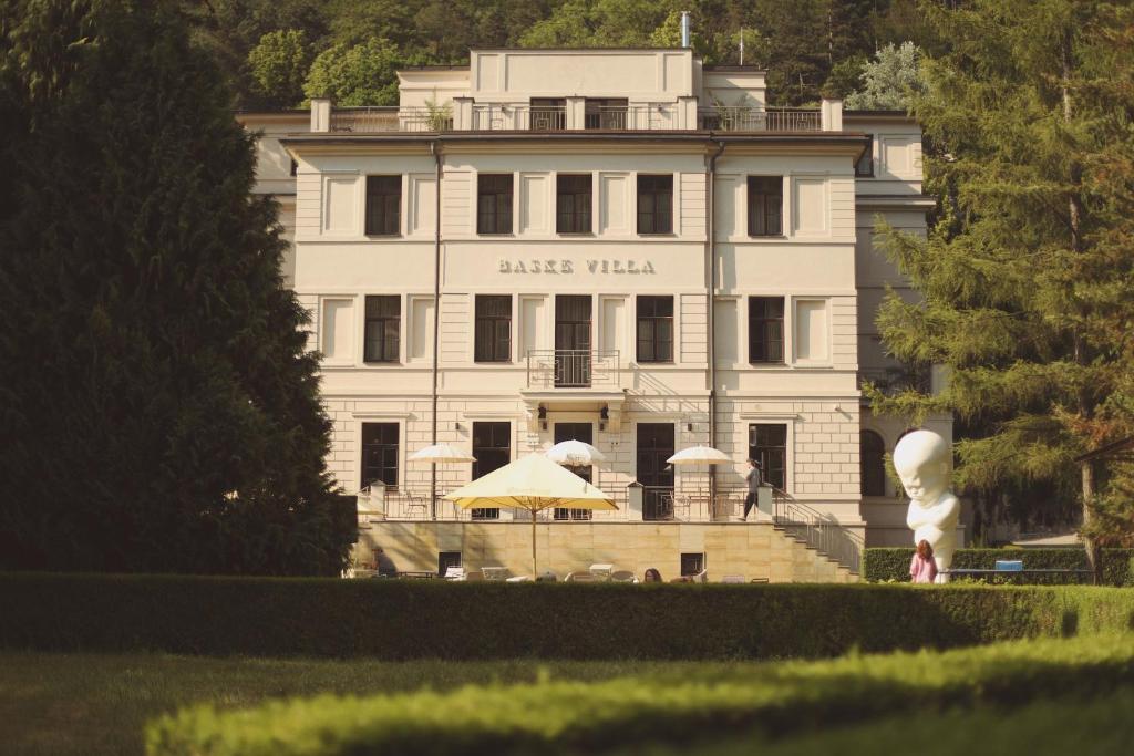 un grande edificio bianco con ombrelloni di fronte di BASKE VILLA a Trenčianske Teplice