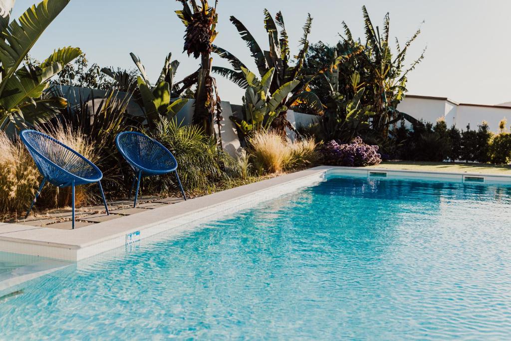 a swimming pool with two blue chairs next to it at Vila Milreu Guest House in Estói