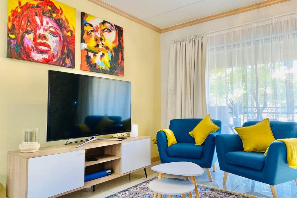 a living room with two blue chairs and a television at Phoenix Rising Apartment in Midrand