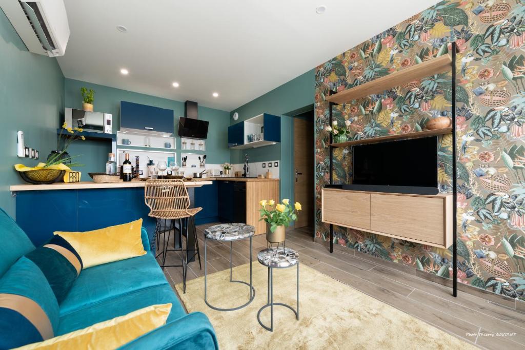 a living room with a blue couch and a kitchen at Le Marchand De Sable - Maisonnette climatisée classée 4 étoiles - 2 Personnes - Plage de la Grande Conche à 200m - ROYAN in Royan