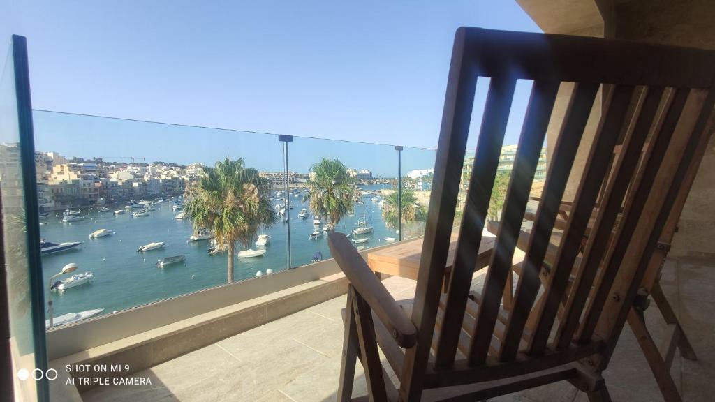 een houten stoel op een balkon met uitzicht op een haven bij Aquamarine Sea Front Apartments - Third Floor in Marsaskala