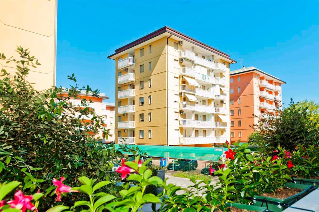 a tall apartment building with a pool and flowers at Apartments in Bibione 24576 in Bibione