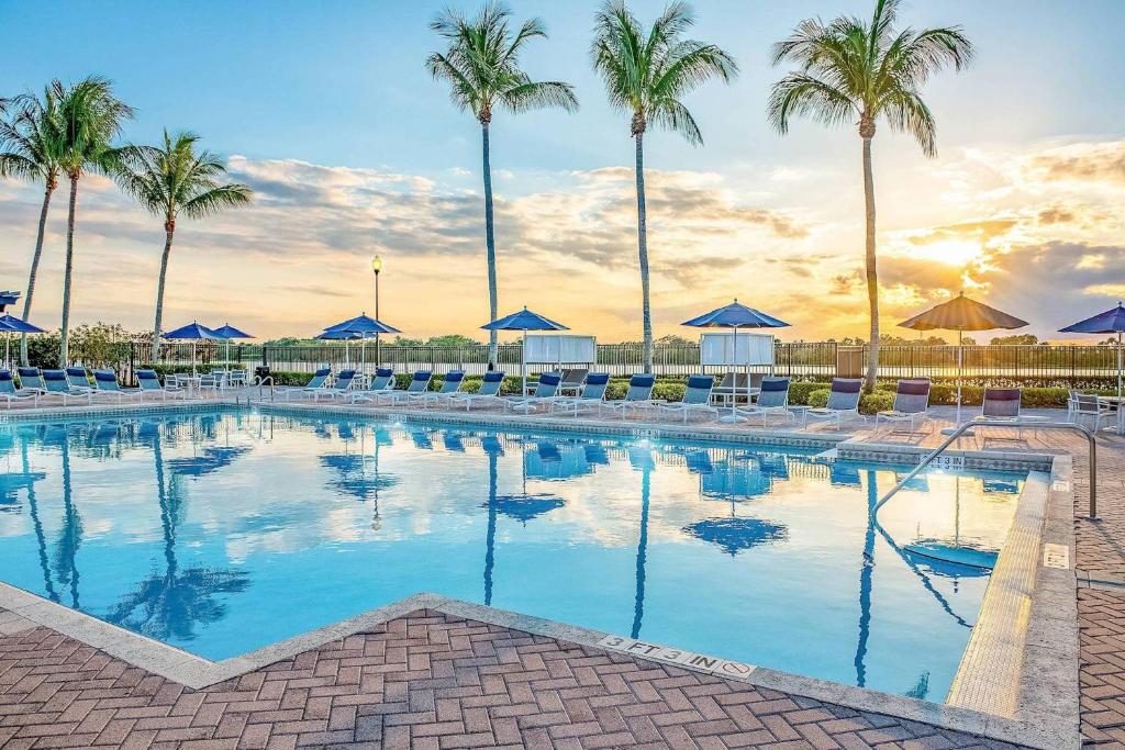 una gran piscina con palmeras y sombrillas azules en Kasa Wellington South Florida en Wellington